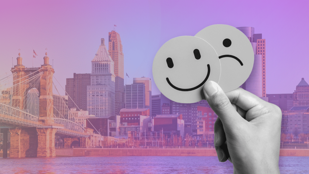In the background, Cincinnati's skyline is in a rainbow gradient. The foreground is a smile and frown in black and white.