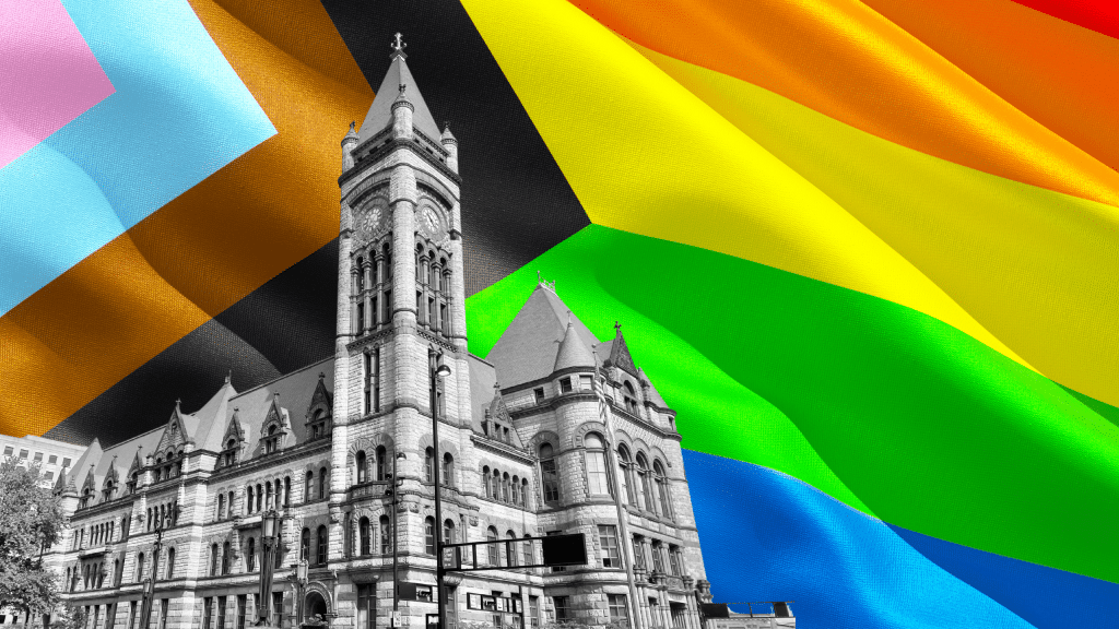 Cincinnati City Hall building is superimposed in black-and-white in front of the LGBTQ+ Progress flag.
