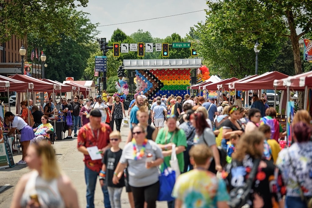 Crowds of people are in a street celebrating Springfield Pride with an LGBTQ+ flag in the background.