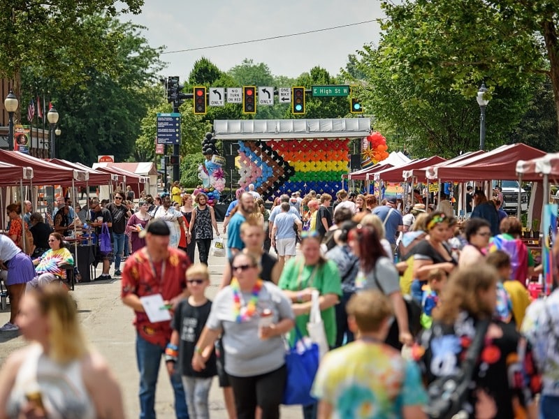 Crowds of people are in a street celebrating Springfield Pride with an LGBTQ+ flag in the background.